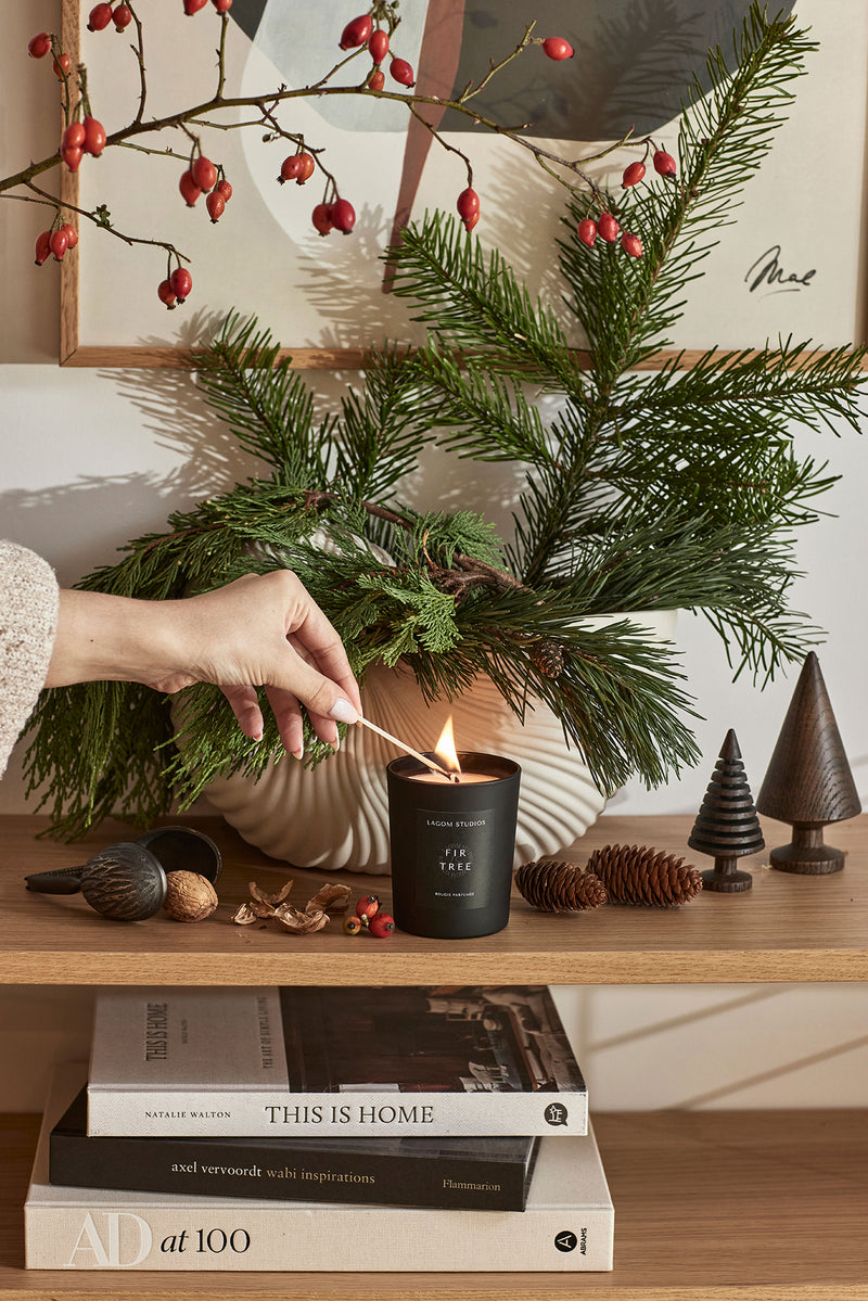 Lagom Studios schwarze Duftkerze wird angezündet_Steht auf Eichen String Regal_Streichholz mit Feuer und weihnachtlicher Dekoration 